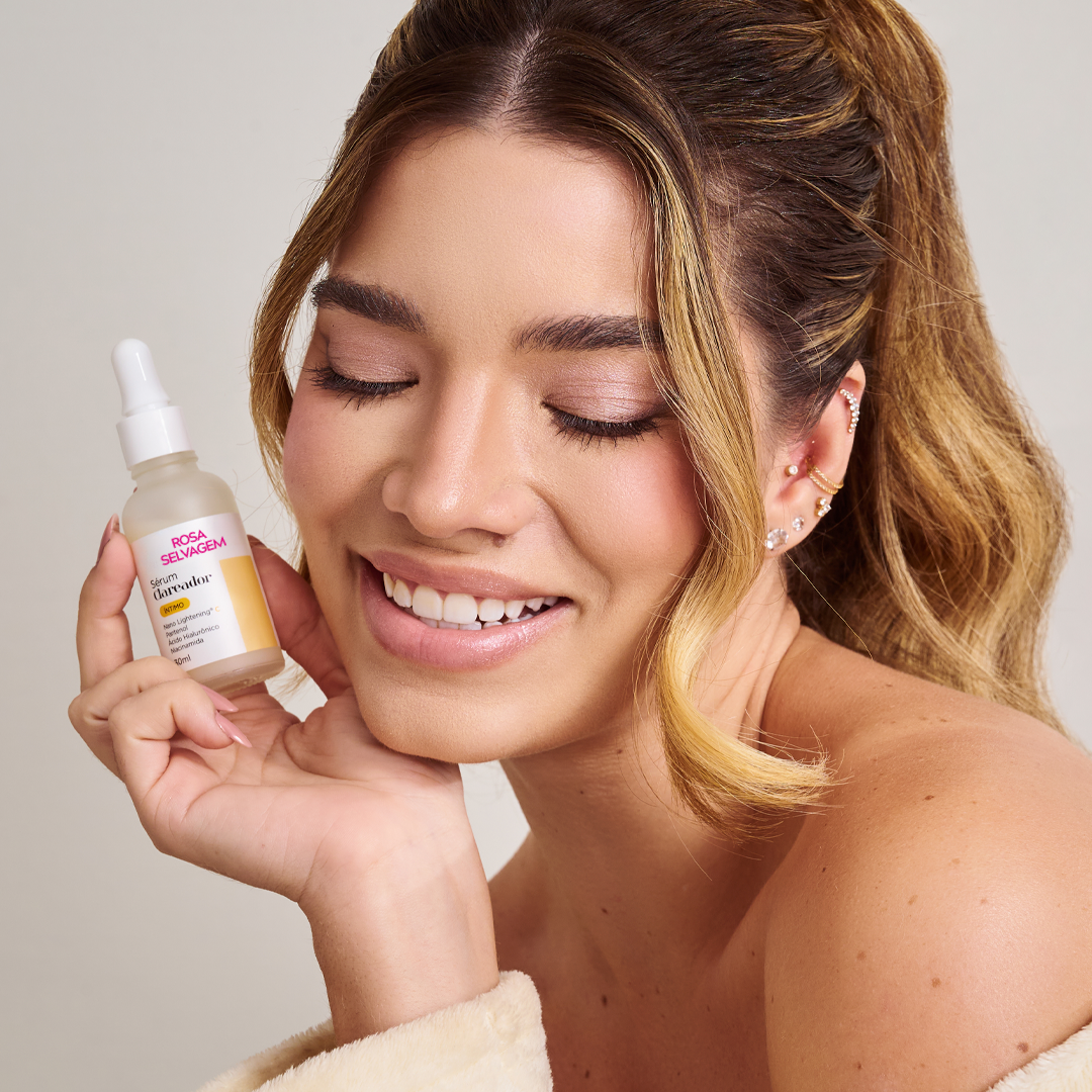 Mulher sorrindo com olhos fechados segurando produto Rosa Selvagem